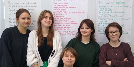 Powiększ grafikę: Pięć uczennic stoi na tle dużego arkusza papieru, na którym napisany jest wiersz w j. angielskim.