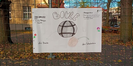 Powiększ grafikę: Na siatce przy boisku szkolnym wisi plakat przedstawiający piłkę do gry w boule.