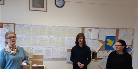 Powiększ grafikę: Uczeń stoi na tle tablicy z planem lekcji. Po jego prawej stronie p. K. Radzikowska, po lewej p. dyr. M. Mroczkowska.