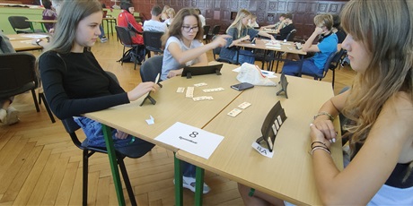Powiększ grafikę: W auli szkolnej uczniowie siedzą przy stolikach i grają w Rummikuba