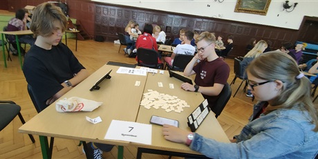 Powiększ grafikę: W auli szkolnej uczniowie siedzą przy stolikach i grają w Rummikuba