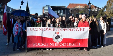Powiększ grafikę: Grupa uczniów w centrum Gdańska trzyma wielki baner w kolorach Polskiej flagi. Na banerze logo szkoły i napis: "Uczniowie Topolówki Polsce niepodległej"