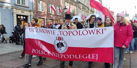Powiększ grafikę: Grupa uczniów podczas marszu w centrum Gdańska trzyma wielki baner w kolorach Polskiej flagi. Na banerze logo szkoły i napis: "Uczniowie Topolówki Polsce niepodległej"