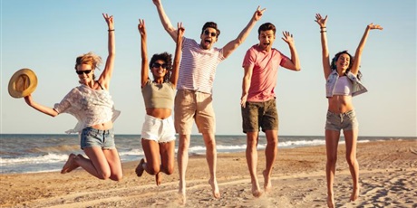 Powiększ grafikę: Zdjęcie 5 osób na plaży. Wszyscy radośnie podskakują z rękami podniesionymi do góry.