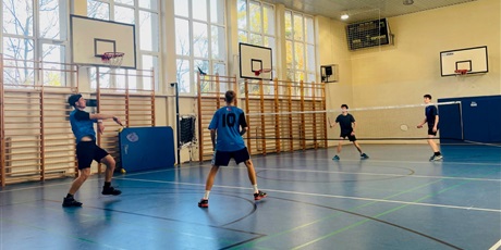Powiększ grafikę: Dwie dwuosobowe drużyny grające w badmintona na sali gimnastycznej. Jedna drużyna stoi tyłem.