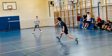 Powiększ grafikę: Dwóch uczniów w czasie meczu badmintona. Z prawej strony pod ścianą zawodnicy innych drużyn obserwują mecz.
