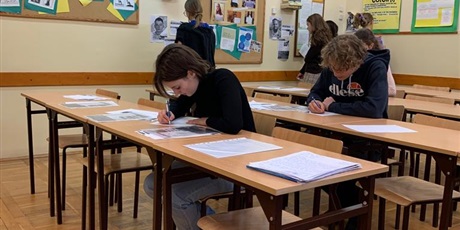 Powiększ grafikę: Zdjęcie uczniów piszących listy (na pierwszym planie). W tle grupa uczniów czytająca zamieszczone na ścianie materiały.