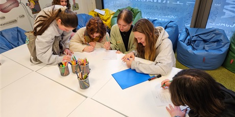 Powiększ grafikę: Grupa uczennic kuca przy stoliku i wypełnia ankiety ewaluacyjne.