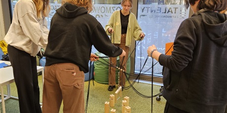 Powiększ grafikę: Uczennice próbują w grupie ustawić wieżę z drewnianych elementów. Każda trzyma sznurek przywiązanych do drewnianego elementu chwytającego.