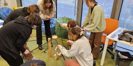 Powiększ grafikę: Uczennice próbują w grupie ustawić wieżę z drewnianych elementów. Każda trzyma sznurek przywiązanych do drewnianego elementu chwytającego.