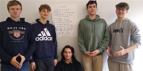 Powiększ grafikę: Pięciu uczniów stoi na tle dużego arkusza papieru, na którym napisany jest wiersz w j. angielskim.