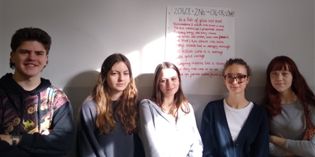 Powiększ grafikę: Pięcioro uczniów stoi na tle dużego arkusza papieru, na którym napisany jest wiersz w j. angielskim.
