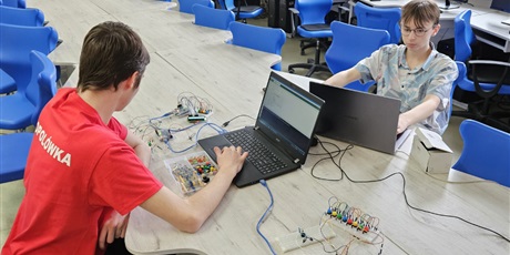 Powiększ grafikę: W pracowni informatycznej dwóch uczniów siedzi przy laptopach. Przed nimi leżą elementy elektroniczne.