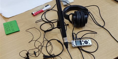 Powiększ grafikę: Na ławce leży sprzęt niezbędny do nagrania: słuchawki, mikrofon, dyktafon.
