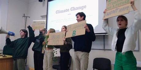 Powiększ grafikę: Grupa uczniów odgrywająca scenę protestu: jedna uczennica trzyma tubę, pozostałe osoby mają różne hasła wypisane na kartonowych planszach.