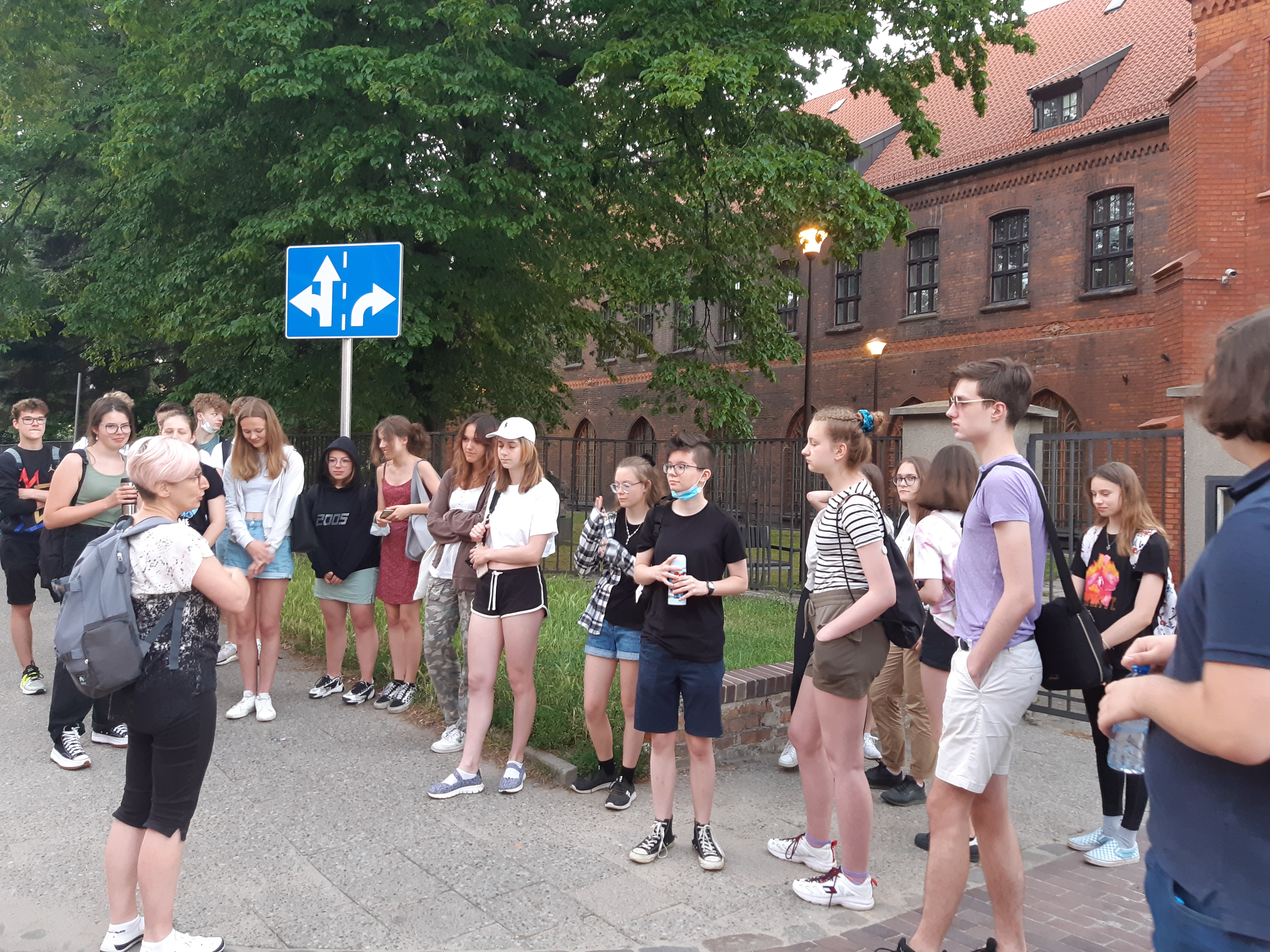Zdjęcie grupy uczniów słuchających przewodniczki przed budynkiem Muzeum Narodowego w Gdańsku.