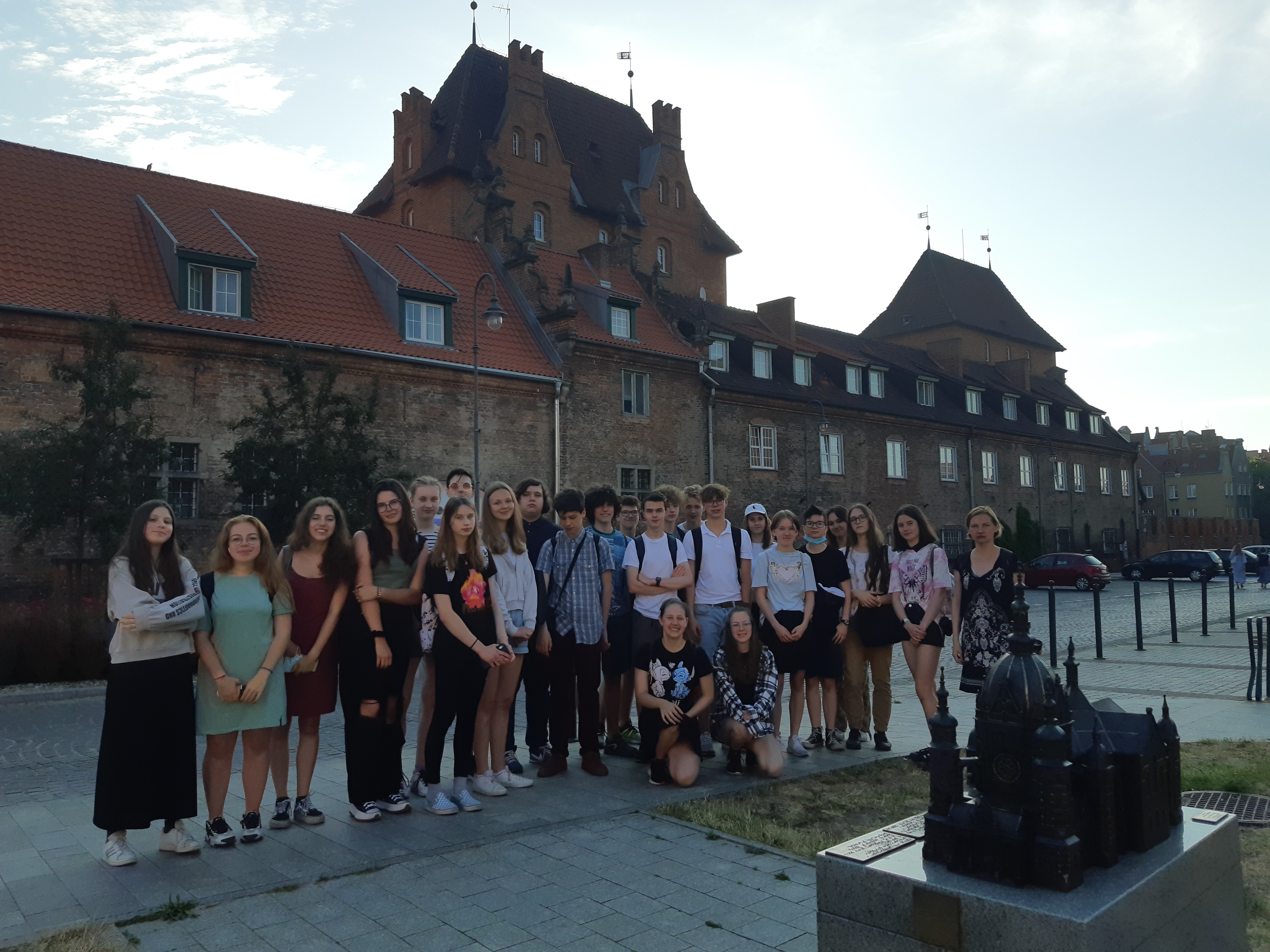 Zdjęcie grupy uczniów słuchających przewodniczki podczas zwiedzania Gdańska.