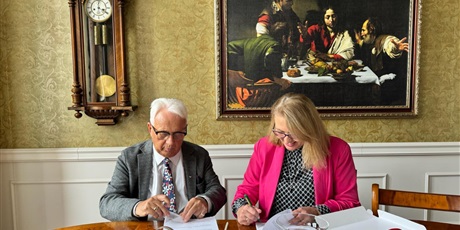 Powiększ grafikę: Pani Dyrektor Topolówki i pan Rektor Ateneum siedzą przy stole. Podpisują porozumienie o współpracy.